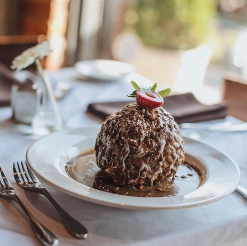 A decadent chocolate dessert topped with a strawberry and mint, served on a white plate with a rich sauce.