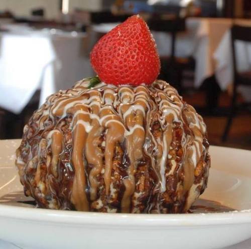 A dessert ball drizzled with chocolate and caramel sauce, topped with a fresh strawberry, served on a white plate.