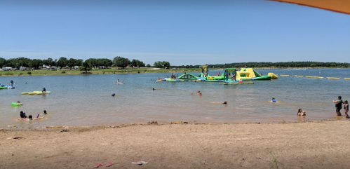 A sunny beach scene with people swimming and playing on inflatable structures in a lake.