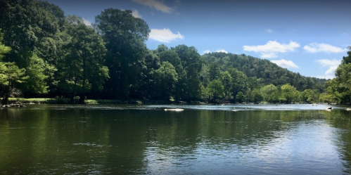 A serene river scene surrounded by lush green trees and hills under a clear blue sky.