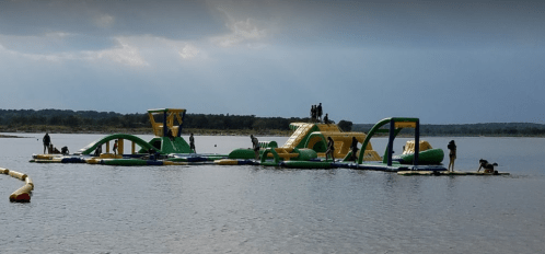 A colorful inflatable water park with slides and obstacles, set on a lake with people enjoying the activities.