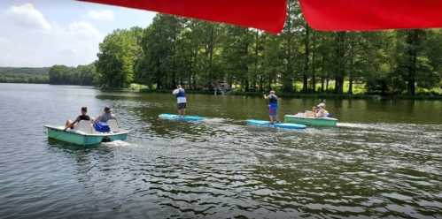 Four people enjoy a sunny day on a lake, paddling in small boats surrounded by lush greenery.