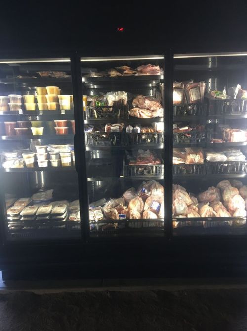A refrigerated display case filled with various packaged meats and prepared food items.