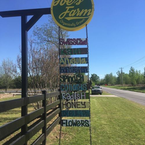 Sign at Joe's Farm listing organically grown produce: Swiss Chard, Kale, Arugula, Basil, Spinach, Corn, Radish, Honey, Flowers.