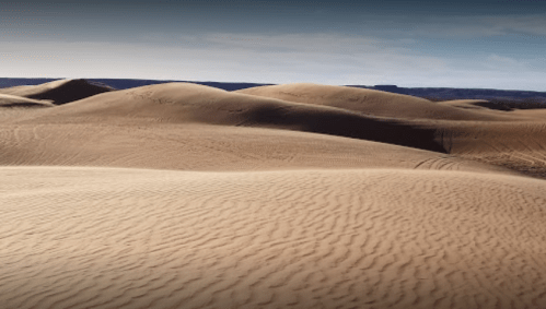 A vast desert landscape with rolling sand dunes under a clear blue sky.