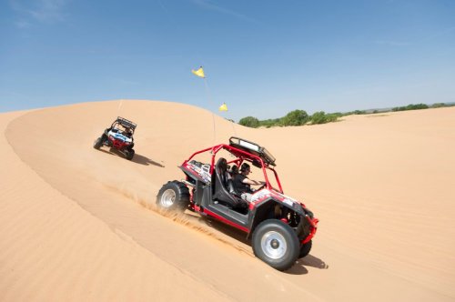 Two off-road buggies racing down a sandy dune under a clear blue sky.