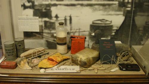 Display of washed-up maritime artifacts, including bottles, cans, and a guide on abandoning a ship.
