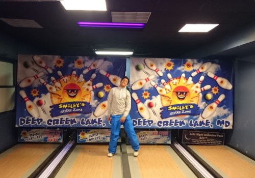 A person poses in front of bowling lanes with colorful banners at Smiley's Strike Zone in Deep Creek Lake, MD.