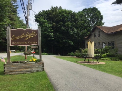 Sign for "Candlelight Housekeeping Cottages" beside a gravel driveway, with greenery and a cottage in the background.
