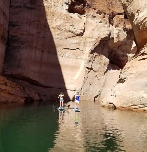 Two people paddleboarding in a narrow canyon with towering rock walls and calm green water.
