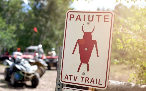 Sign for Paiute ATV Trail featuring a red bull graphic, with ATVs visible in the background.