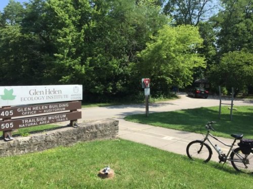 Sign for Glen Helen Ecology Institute with a bike parked nearby, surrounded by greenery and a pathway leading into the woods.