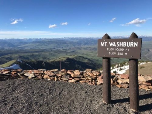 Sign for Mt. Washburn at 10,219 ft elevation, with a panoramic view of mountains and valleys in the background.