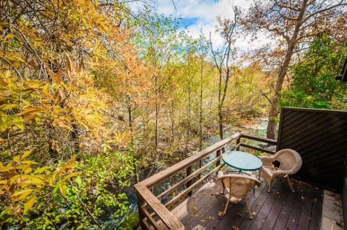 A cozy balcony with a glass table and chairs, surrounded by vibrant autumn foliage and a flowing creek below.