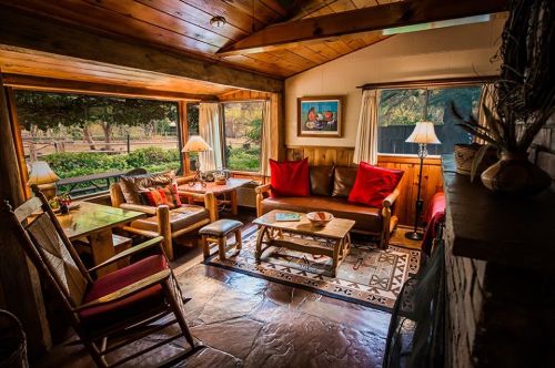 Cozy living room with wooden beams, comfortable seating, and large windows overlooking a green landscape.