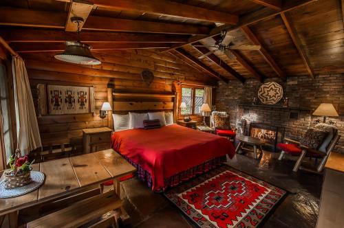 Cozy cabin interior featuring a wooden bed, red bedding, rustic furniture, and a stone fireplace. Warm, inviting atmosphere.