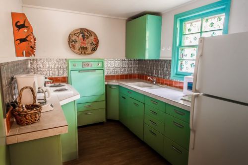 A retro kitchen with mint green cabinets, a silver backsplash, and a window with colorful trim.