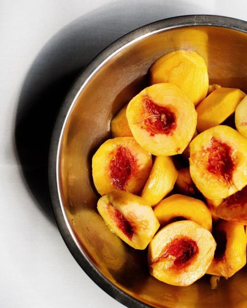 A metal bowl filled with sliced peaches, showcasing their vibrant yellow flesh and red centers.