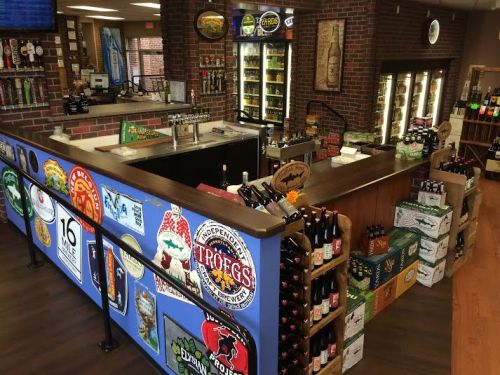 A well-stocked bar with various beer brands, bottles, and a brick wall backdrop in a cozy setting.