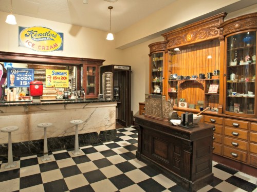Vintage ice cream parlor with a marble counter, wooden display cabinets, and black-and-white checkered floor.