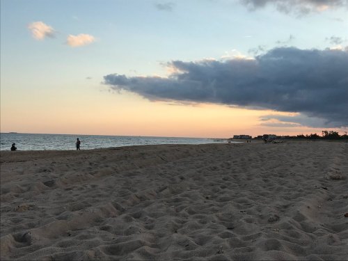 A serene beach at sunset, with gentle waves and a cloudy sky, featuring a few people in the distance.