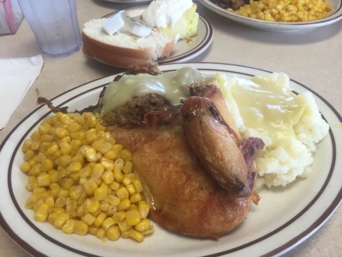 A plate of food featuring roasted chicken, mashed potatoes with gravy, corn, and a slice of bread.
