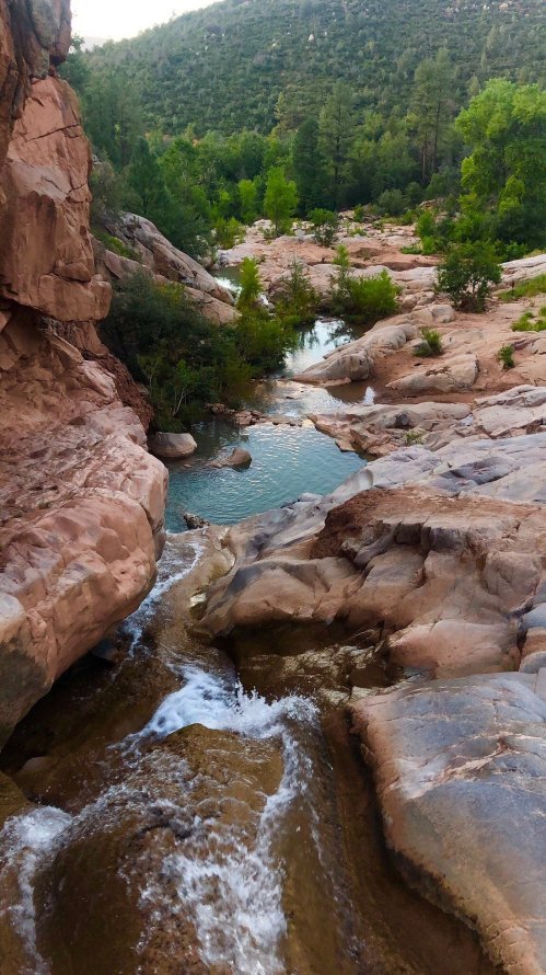 A serene landscape featuring a rocky stream flowing through lush greenery and hills under a clear sky.