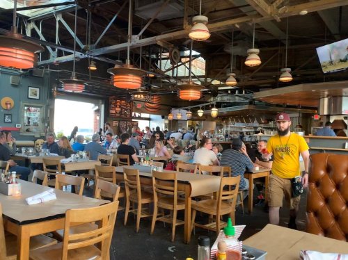 A bustling restaurant interior with diners at wooden tables, industrial decor, and warm lighting.