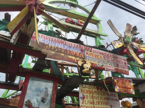 Colorful, eclectic structure with signs celebrating Disney, anniversaries, and various countries, featuring a Mickey Mouse figure.