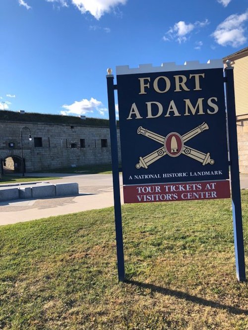 Sign for Fort Adams, a National Historic Landmark, with a view of the fort and blue sky in the background.