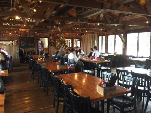 A rustic restaurant interior with wooden tables, chairs, and a festive tree, featuring diners enjoying their meals.