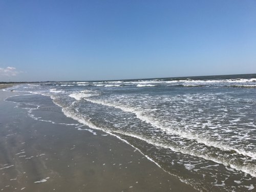 Waves gently lapping on a sandy beach under a clear blue sky.