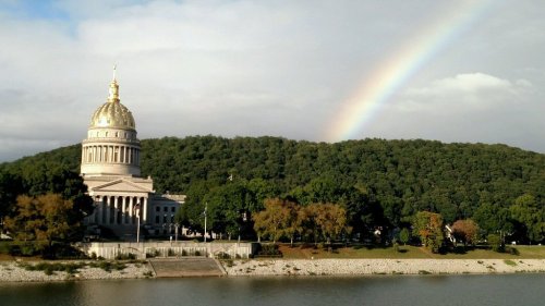 A golden-domed building beside a river, with a rainbow arching over a green hillside in the background.
