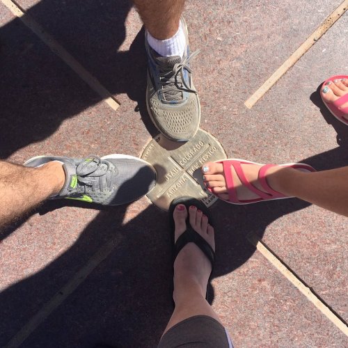 Four pairs of feet on a plaque marking the Four Corners, with different types of footwear on a sunny day.
