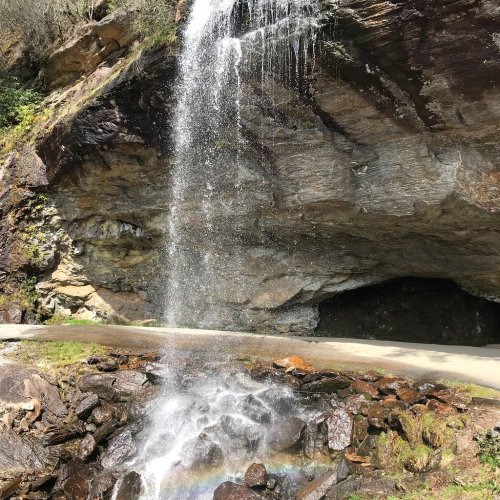 A waterfall cascading over rocky cliffs, creating a mist with a rainbow at the base, surrounded by lush greenery.