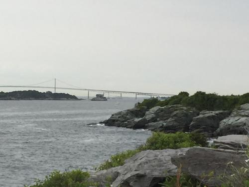 A rocky shoreline with a bridge in the background and a boat on the water under a cloudy sky.