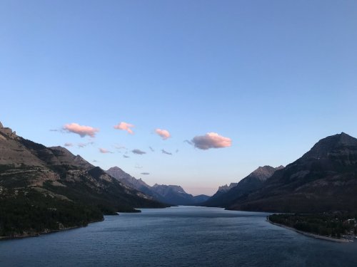A serene landscape featuring a river surrounded by mountains under a clear sky with a few pink clouds.