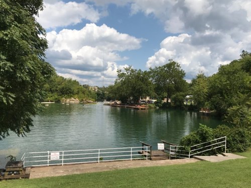 A serene river scene with lush greenery, cloudy skies, and a wooden dock leading to the water.