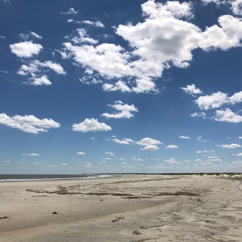 A serene beach scene with soft sand, gentle waves, and a bright blue sky dotted with fluffy white clouds.