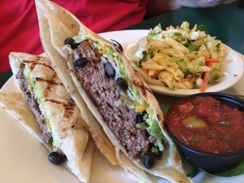 Two grilled tacos filled with beef, black beans, and guacamole, served with a side of coleslaw and salsa.
