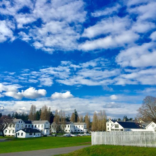 A scenic view of white houses under a bright blue sky with fluffy clouds and green grass in the foreground.