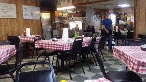 A cozy diner with checkered tablecloths, empty tables, and a visible kitchen area in the background.