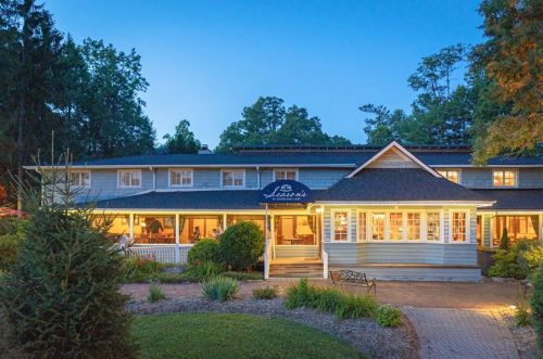 A charming lodge at dusk, featuring warm lights, surrounded by greenery and a welcoming entrance.