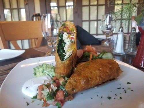 A plate featuring two crispy, stuffed tortillas with salad, guacamole, and salsa on the side, set in a dining environment.