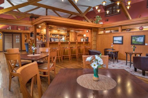 Cozy restaurant interior with wooden beams, a bar, and tables adorned with flower vases. Warm, inviting atmosphere.