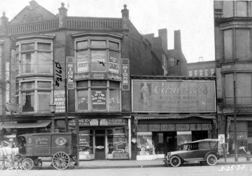 Historic street scene featuring vintage storefronts, a horse-drawn carriage, and early 20th-century automobiles.