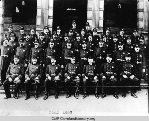A historical black-and-white photo of a large group of uniformed police officers from 1897, posed in front of a building.