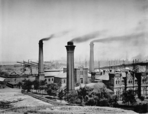 Black and white photo of an industrial complex with smokestacks and surrounding trees, showcasing early manufacturing.