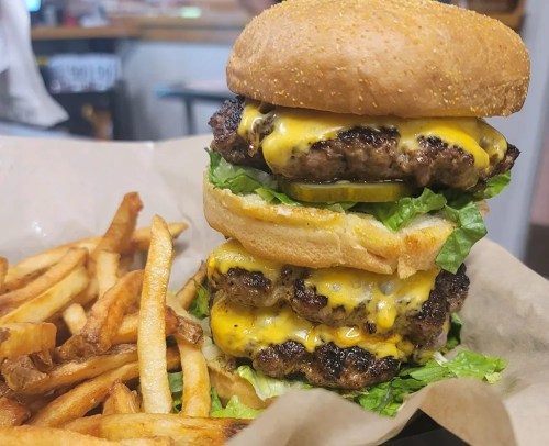 A towering cheeseburger with three beef patties, melted cheese, lettuce, and a sesame seed bun, served with fries.