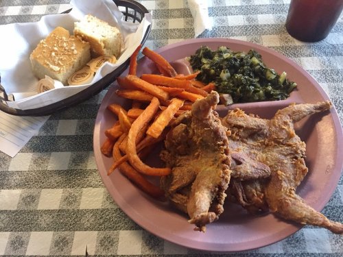 A plate of fried chicken, sweet potato fries, collard greens, and cornbread on a checkered tablecloth.